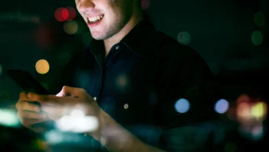 Jovem adulto sorrindo enquanto usa smartphone à noite em ambiente urbano
