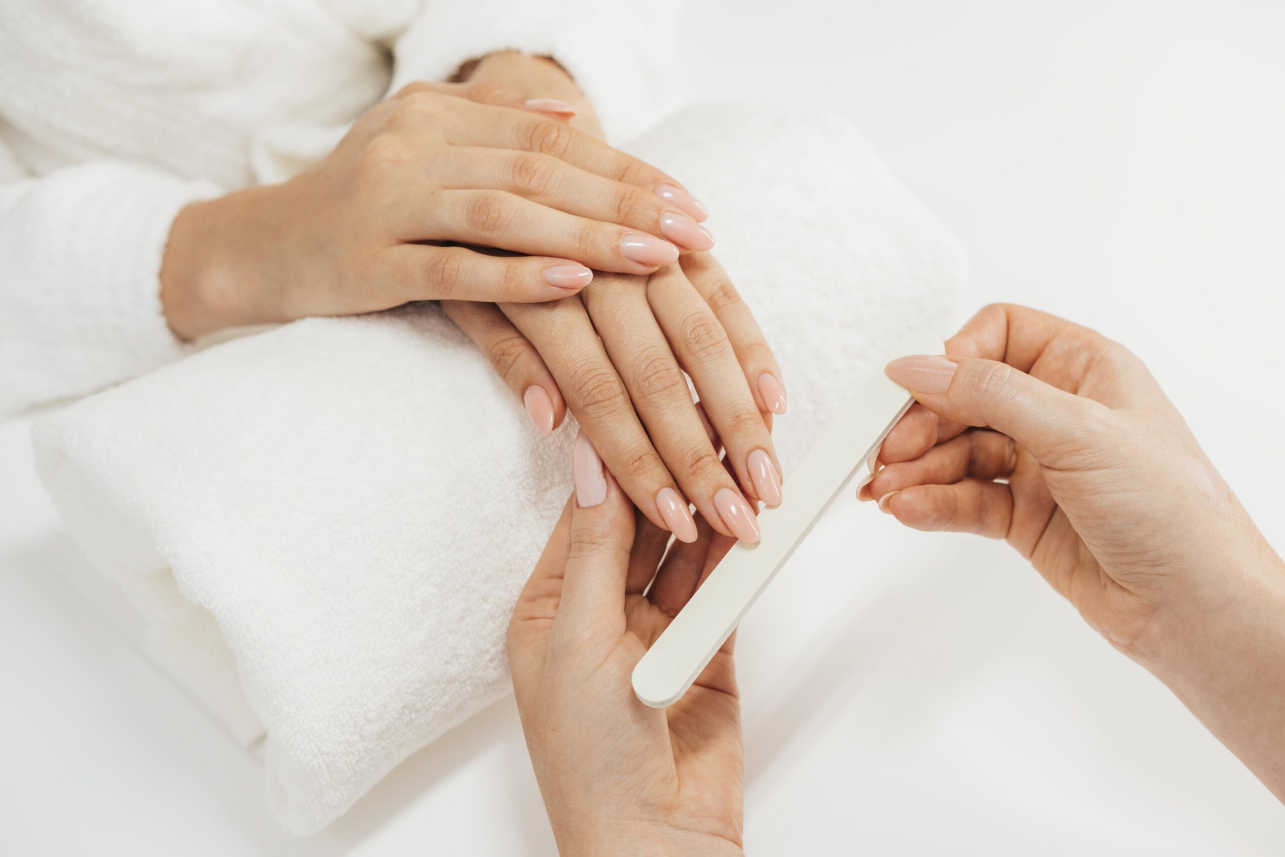 Manicure realizando o processo de modelagem e cuidado nas unhas de uma cliente, com unhas bem cuidadas e saudáveis.