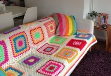 Sofá branco com manta de crochê colorida e almofada listrada, em uma sala moderna e aconchegante