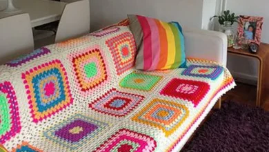 Sofá branco com manta de crochê colorida e almofada listrada, em uma sala moderna e aconchegante