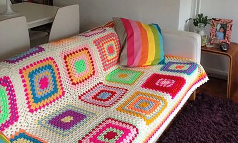 Sofá branco com manta de crochê colorida e almofada listrada, em uma sala moderna e aconchegante