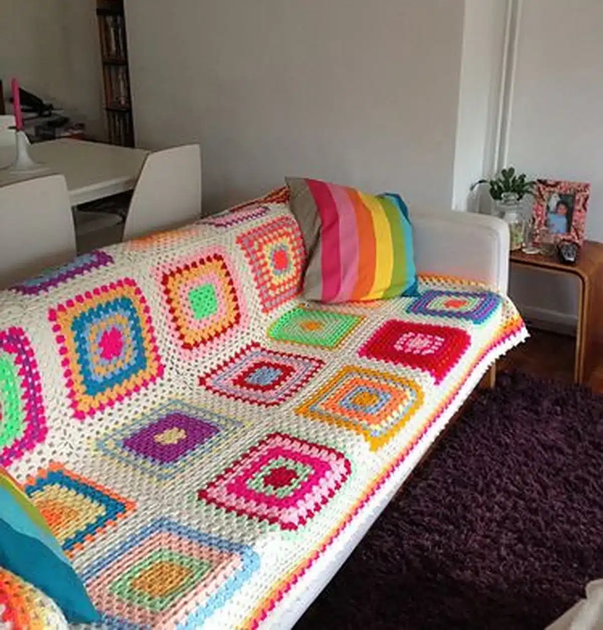 Sofá branco com manta de crochê colorida e almofada listrada, em uma sala moderna e aconchegante