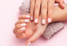 Manicure com esmalte nude brilhante em mãos femininas bem cuidadas sobre toalha texturizada.
