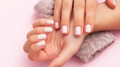 Manicure com esmalte nude brilhante em mãos femininas bem cuidadas sobre toalha texturizada.