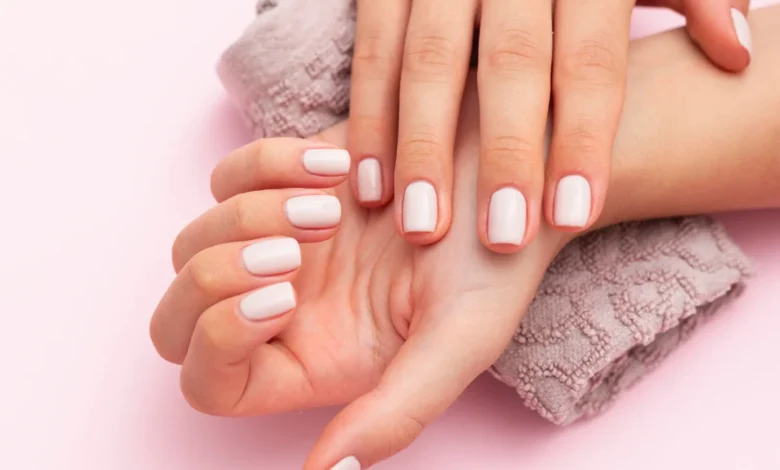 Manicure com esmalte nude brilhante em mãos femininas bem cuidadas sobre toalha texturizada.