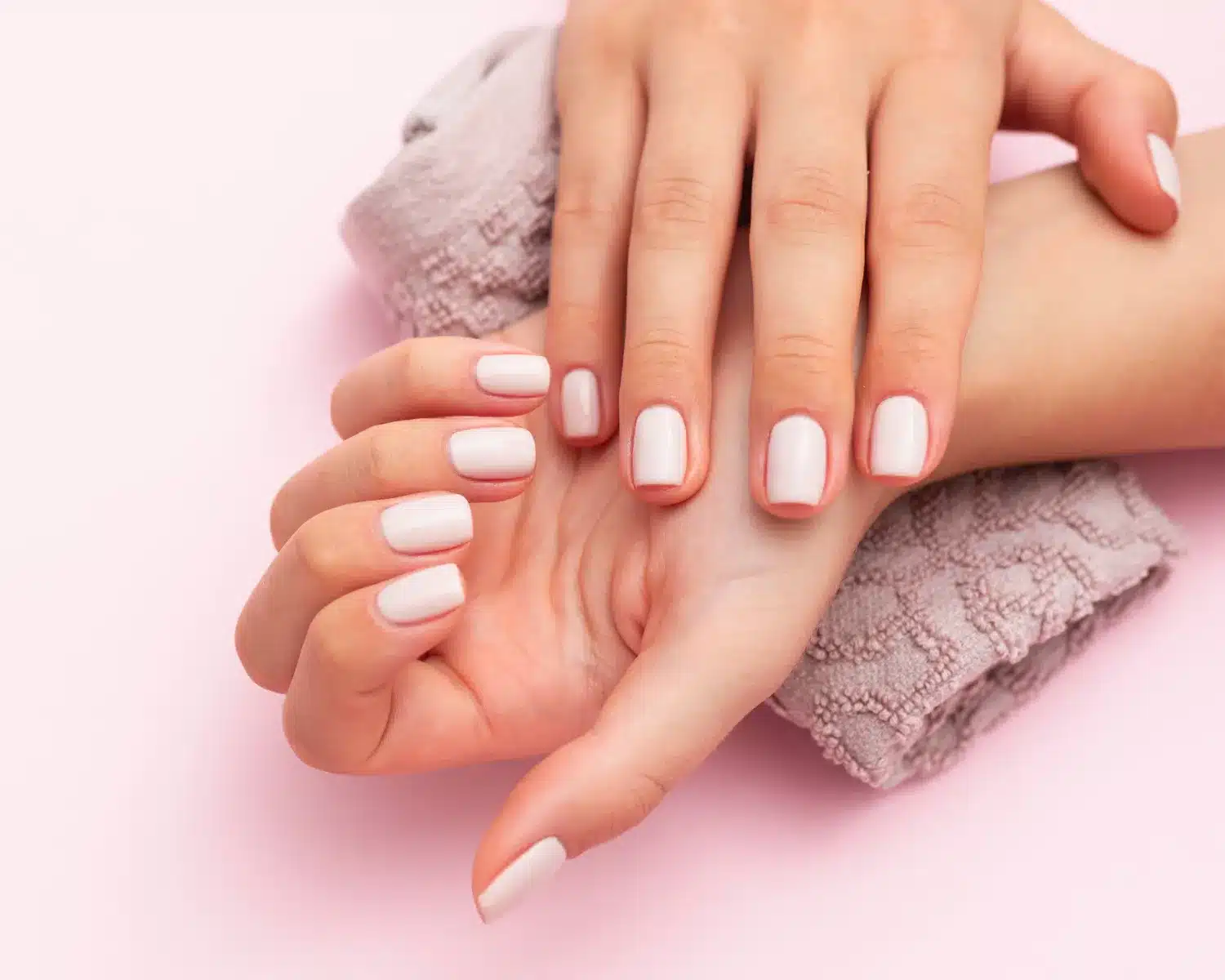 Manicure com esmalte nude brilhante em mãos femininas bem cuidadas sobre toalha texturizada.