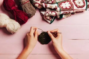 Pessoa fazendo crochê com agulha e fio, iniciando um quadradinho em fundo rosa