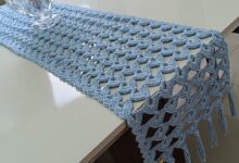 Trilho de mesa em crochê azul claro decorando uma mesa branca.