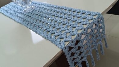 Trilho de mesa em crochê azul claro decorando uma mesa branca.