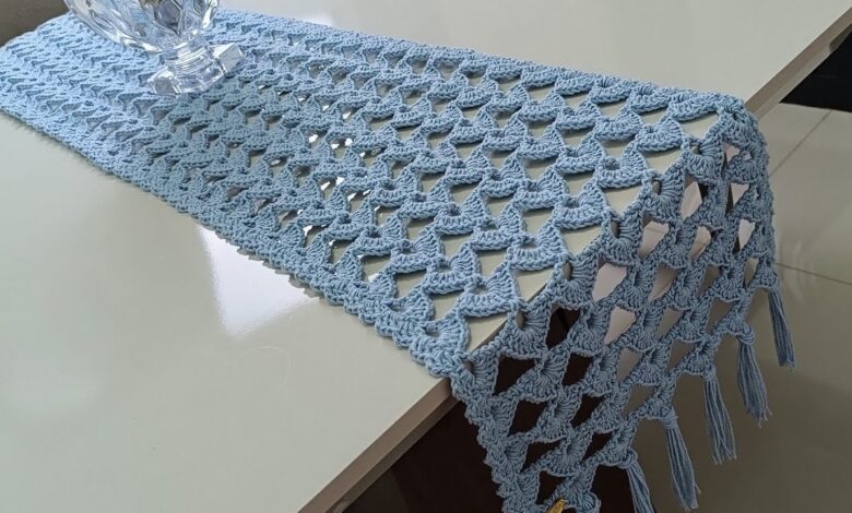 Trilho de mesa em crochê azul claro decorando uma mesa branca.
