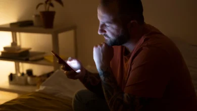 Homem sentado na cama à noite olhando para o celular, preparando-se para enviar uma mensagem de boa noite.