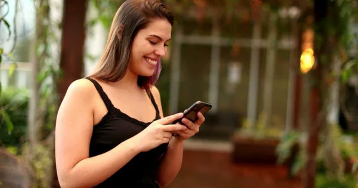Mulher feliz lendo mensagem de fim de semana no celular ao ar livre