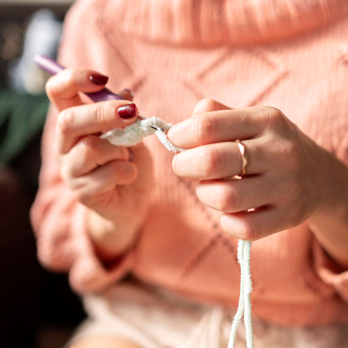 Mãos de mulher segurando agulha e fio, começando um trabalho de crochê em ambiente acolhedor.