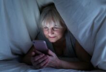 Mulher madura usando smartphone debaixo do cobertor durante a noite.