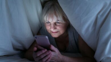 Mulher madura usando smartphone debaixo do cobertor durante a noite.