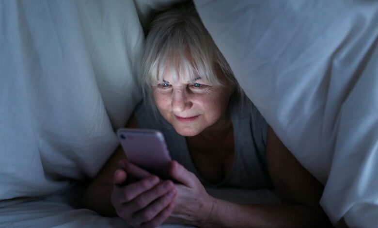 Mulher madura usando smartphone debaixo do cobertor durante a noite.