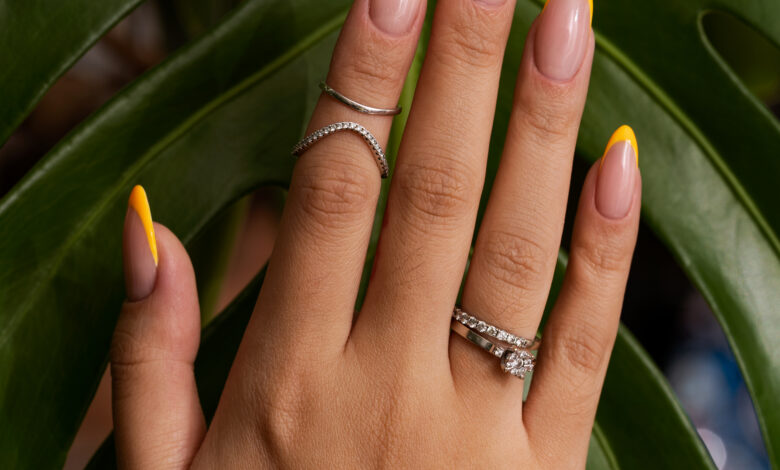 Unhas com francesinha moderna em amarelo vibrante com fundo de folhas verdes tropicais.