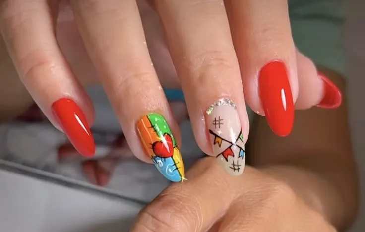 Unhas com nail art colorida e desenhos temáticos de São João, incluindo bandeirinhas e coração