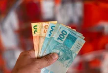 Pessoa segurando cédulas de dinheiro brasileiro com notas de 20, 50 e 100 reais.
