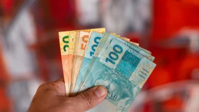 Pessoa segurando cédulas de dinheiro brasileiro com notas de 20, 50 e 100 reais.