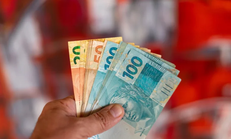 Pessoa segurando cédulas de dinheiro brasileiro com notas de 20, 50 e 100 reais.