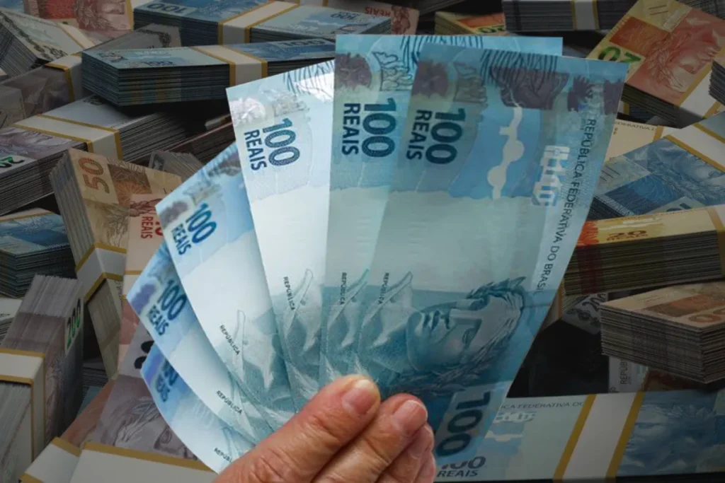 Mão segurando notas de 100 reais, simbolizando o pagamento do 13º do INSS