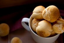 Pães delícia dourados servidos em uma tigela branca sobre uma superfície rústica.