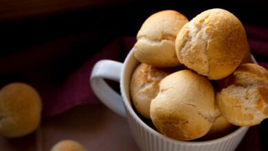 Pães delícia dourados servidos em uma tigela branca sobre uma superfície rústica.