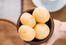 Pão de queijo mineiro sem ovos servido em tigela de madeira, com café ao fundo