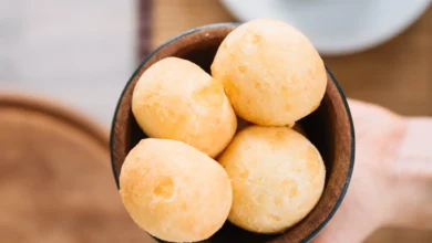 Pão de queijo mineiro sem ovos servido em tigela de madeira, com café ao fundo