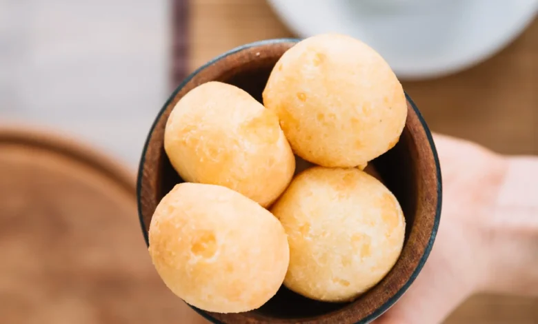 Pão de queijo mineiro sem ovos servido em tigela de madeira, com café ao fundo