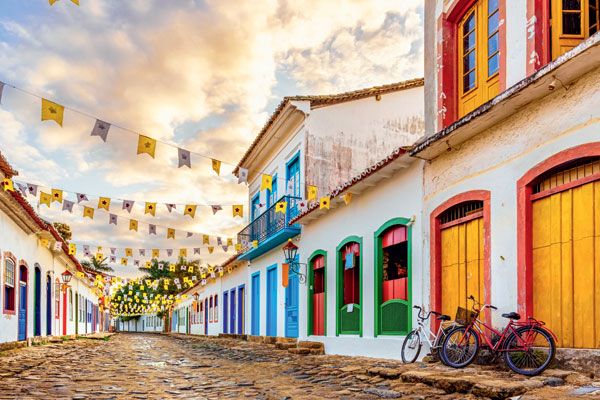 Rua de pedra em Paraty com casas coloridas e bandeirinhas decorativas ao entardecer