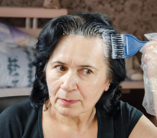 Mulher madura aplicando tintura no cabelo, ilustrando os cuidados com a coloração dos fios.