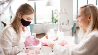 Manicure aplicando esmalte em unhas de uma cliente em um salão de beleza, com foco nos tons de esmalte terrosos.