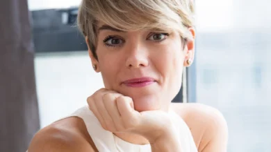 Mulher com corte pixie moderno, sorrindo e inclinando o rosto sobre a mão, mostrando estilo e confiança.