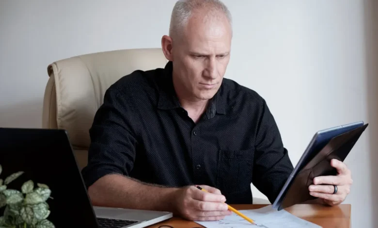 Homem concentrado analisando documentos financeiros com laptop ao lado, simbolizando planejamento financeiro para aposentados em 2025.