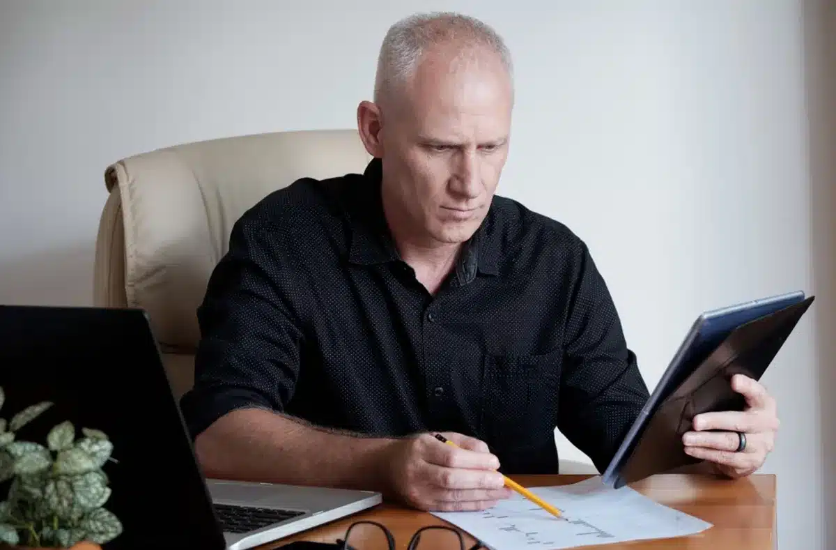 Homem concentrado analisando documentos financeiros com laptop ao lado, simbolizando planejamento financeiro para aposentados em 2025.