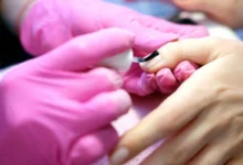 Aplicação de esmalte em gel em unha com profissional usando luvas rosas