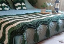 Cama decorada com manta e almofadas em crochê verde e branco, criando um ambiente acolhedor e estiloso.