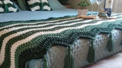 Cama decorada com manta e almofadas em crochê verde e branco, criando um ambiente acolhedor e estiloso.