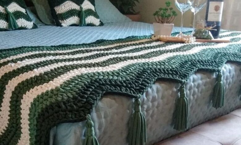Cama decorada com manta e almofadas em crochĂȘ verde e branco, criando um ambiente acolhedor e estiloso.