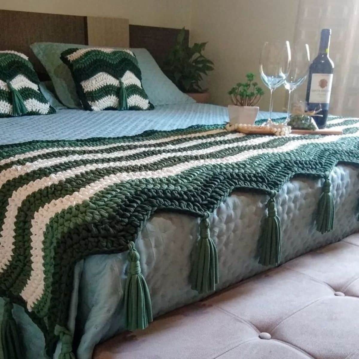 Cama decorada com manta e almofadas em crochê verde e branco, criando um ambiente acolhedor e estiloso.