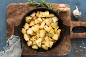 Porção de batatas assadas com ervas servidas em frigideira sobre tábua de madeira