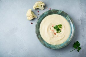 Prato de creme de couve-flor com folhas decorativas e pedaços da hortaliça sobre fundo claro
