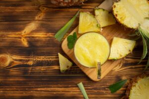 Copo de suco de abacaxi sobre tábua de madeira com pedaços da fruta ao redor