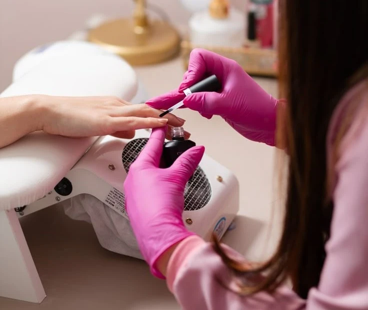 Aplicação de esmalte em gel nas unhas com profissional usando luvas rosas
