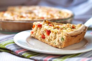 Torta fit de legumes com pedaços coloridos de pimentão e uma crosta dourada, servida em prato branco.