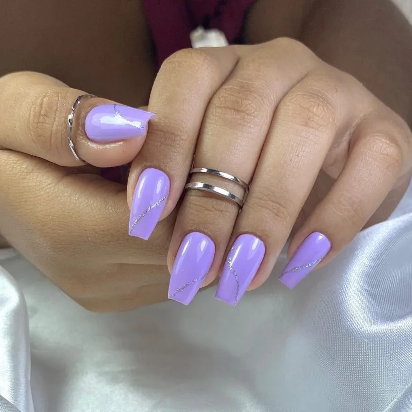 Unhas com formato bailarina, esmalte lilás e detalhes em strass.