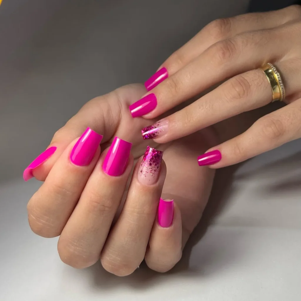Unhas quadradas com esmalte rosa brilhante e detalhes em glitter.