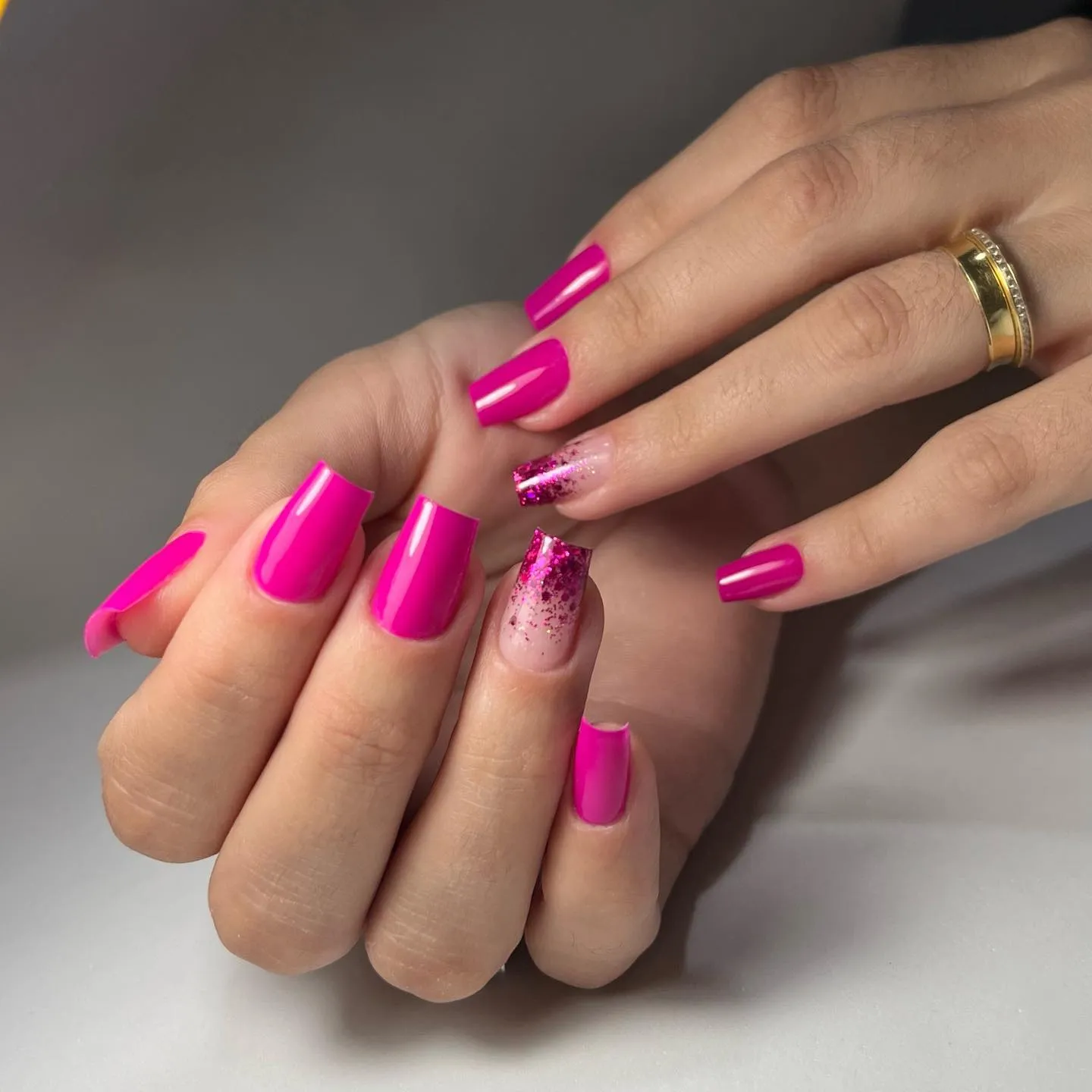 Unhas quadradas com esmalte rosa brilhante e detalhes em glitter.